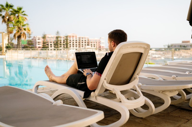 Young man relaxing with his laptop by a pool.