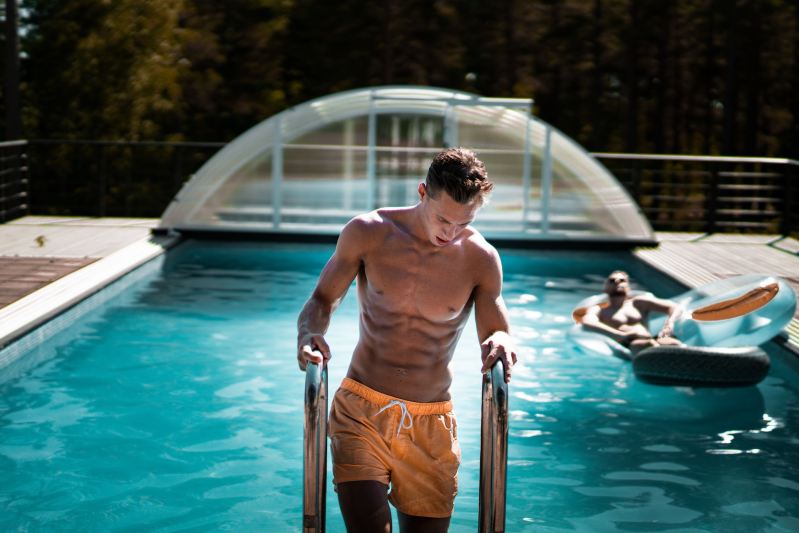 Fit, shirtless man climbing out of swimming pool.