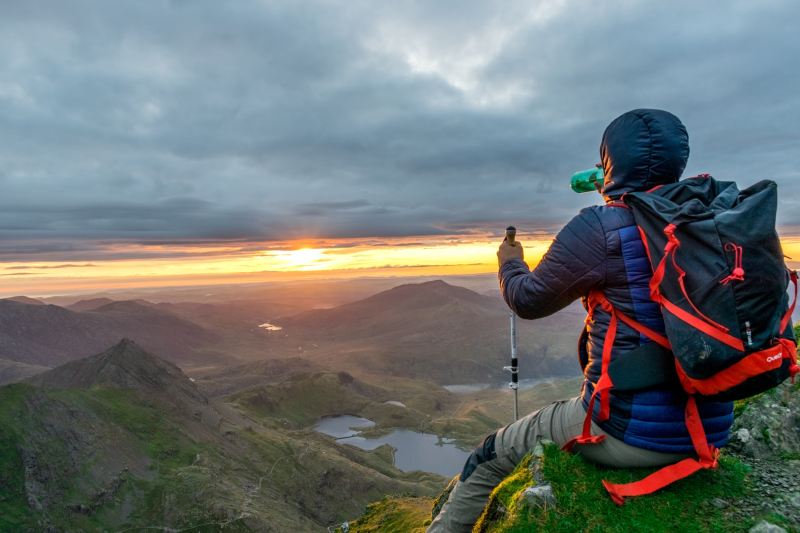 A man sits on a mountain ledge looking out over the sunset.