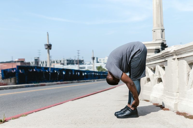 A man in gray shorts stretching on sidewalk