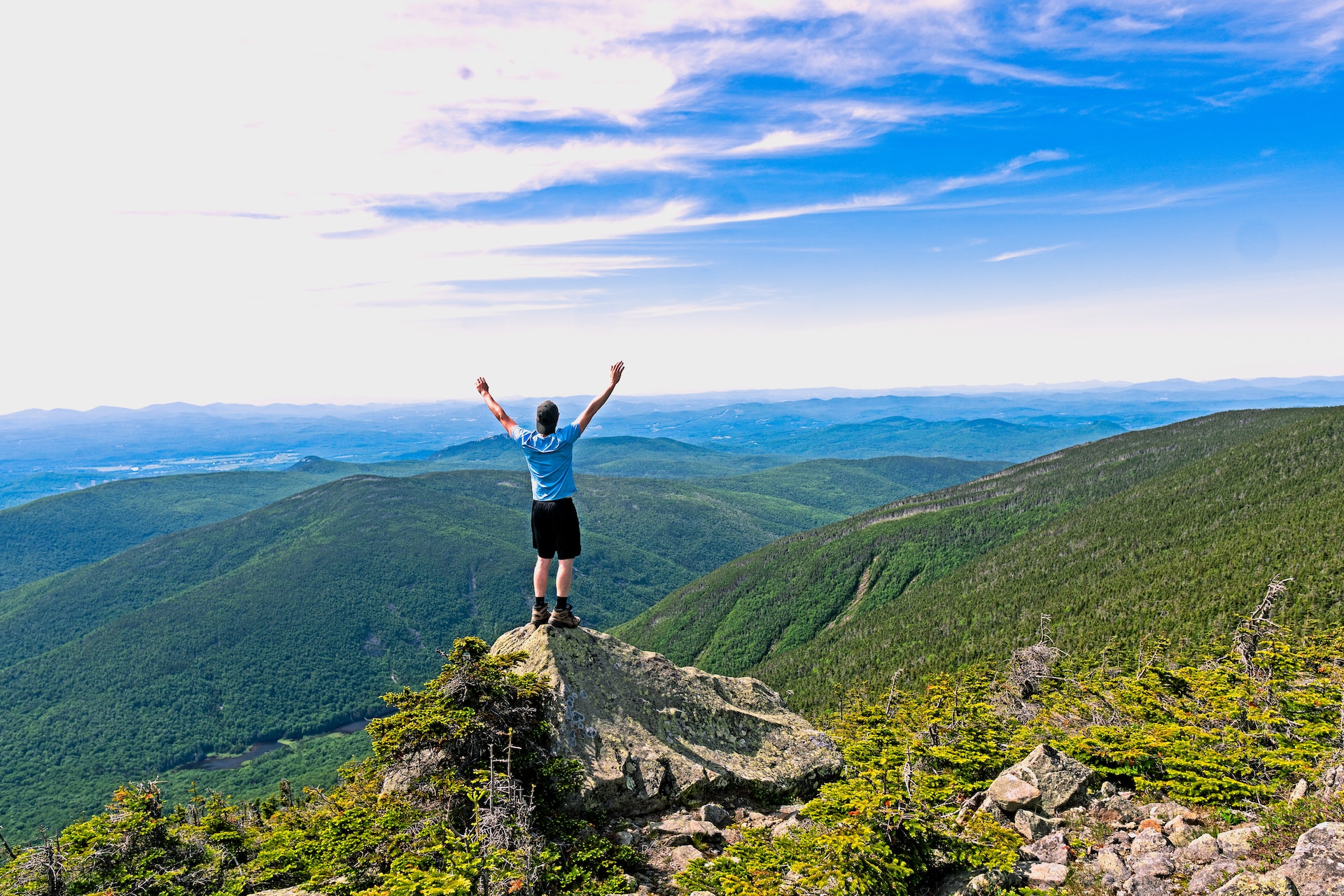Man standing triumphantly atop a peak in New Hampshire's White Mountain National Forest.