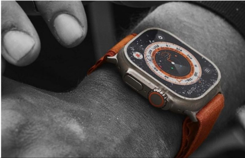 The Apple Watch Ultra covered in just a touch of sand on the arm of a man doing tough work.