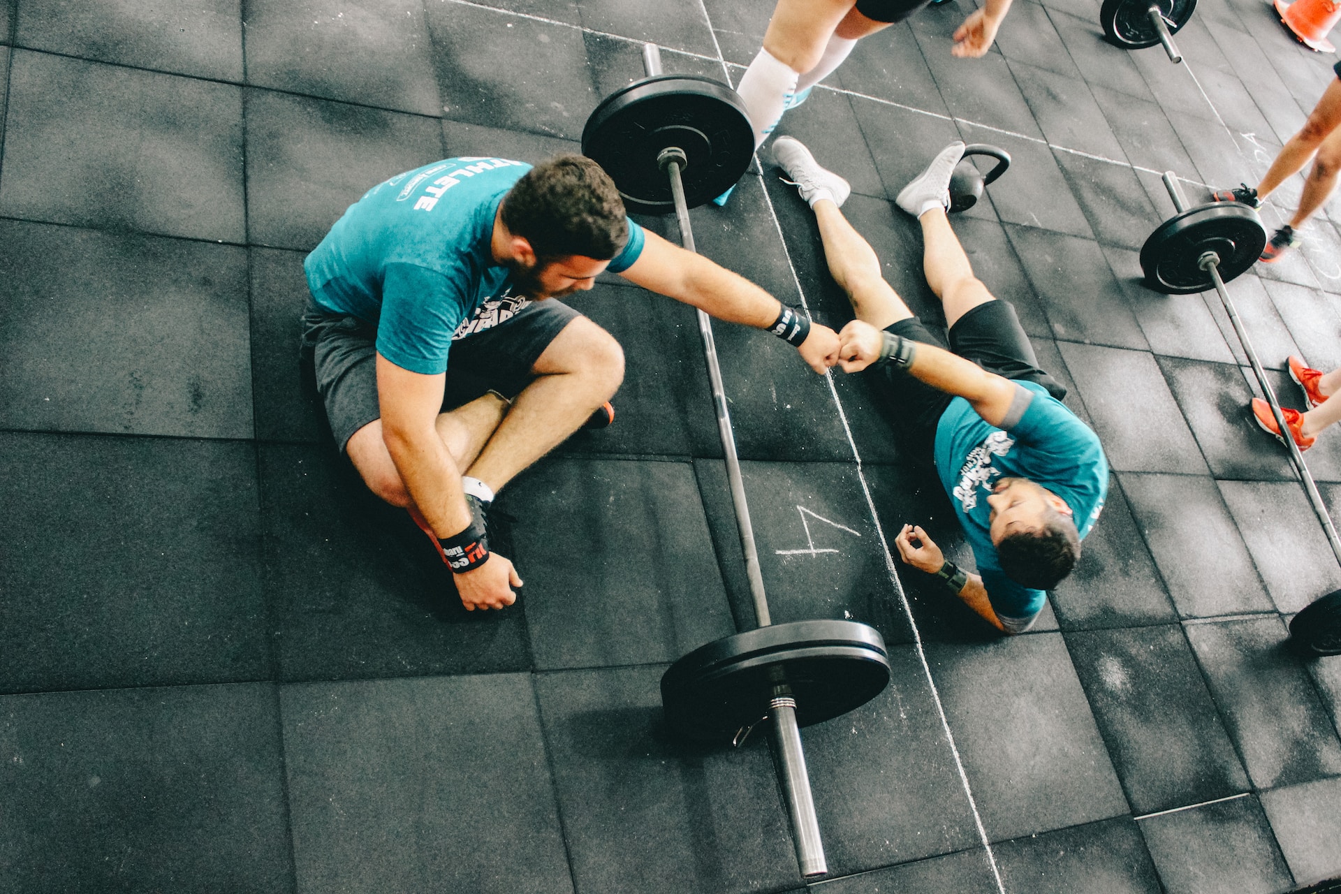 Man fist-bumping his personal trainer over a barbell.
