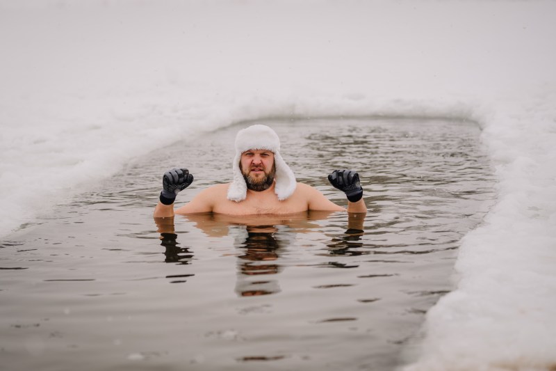 Man wearing a white hat and black gloves swimming in a hole in the ice