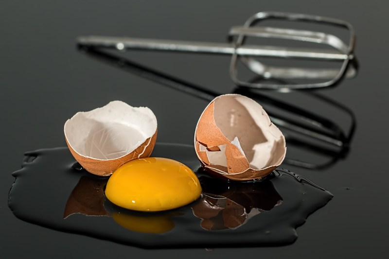Huevo roto con un batidor de huevos sobre una superficie negra