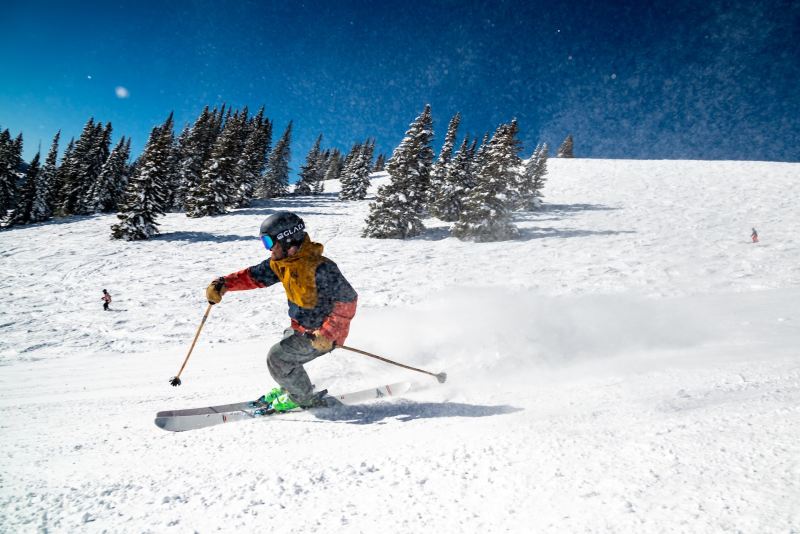 A man skis on a clear run, with mountains and trees behind him.