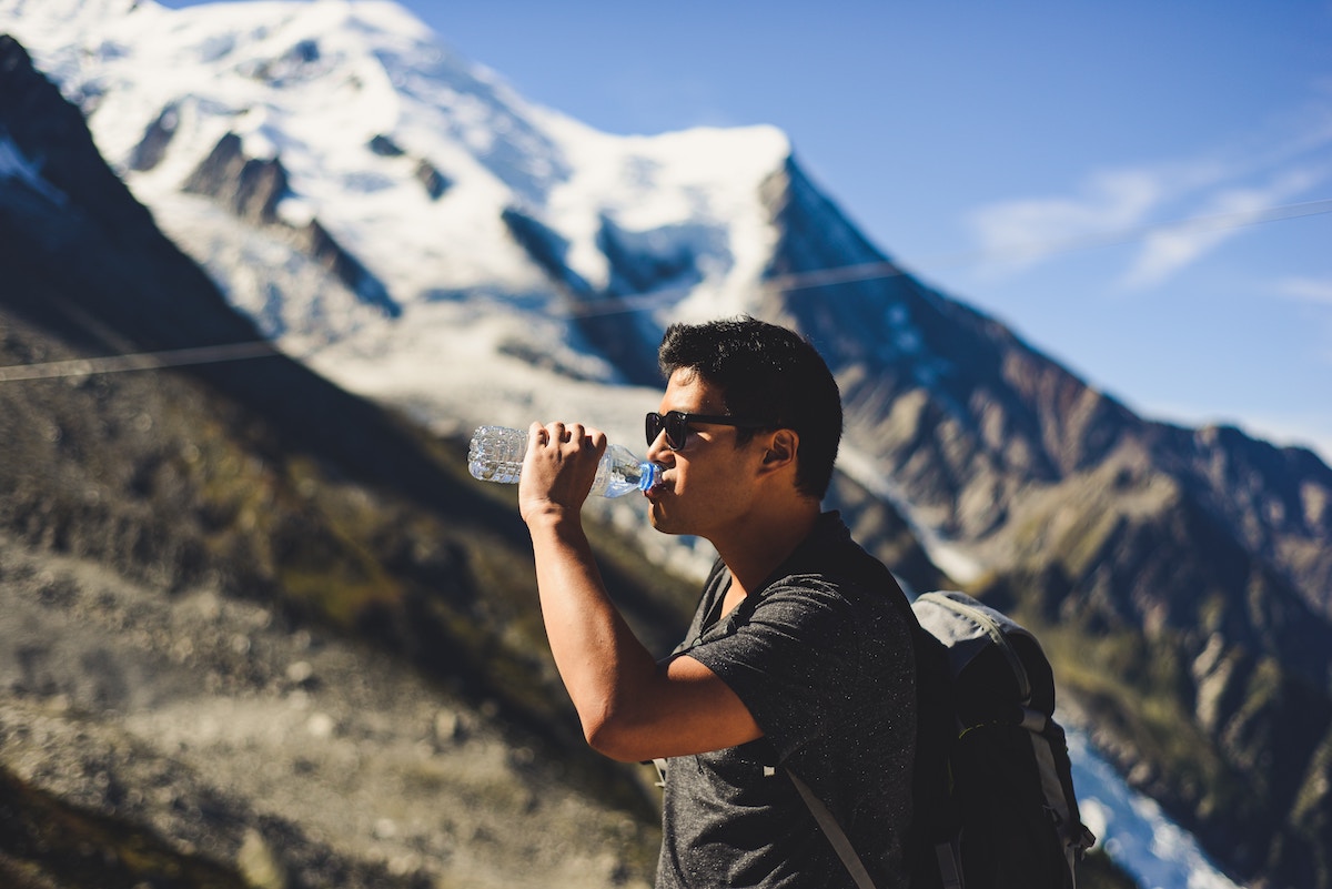 Un hombre bebiendo de una botella de agua grande cerca de una montaña