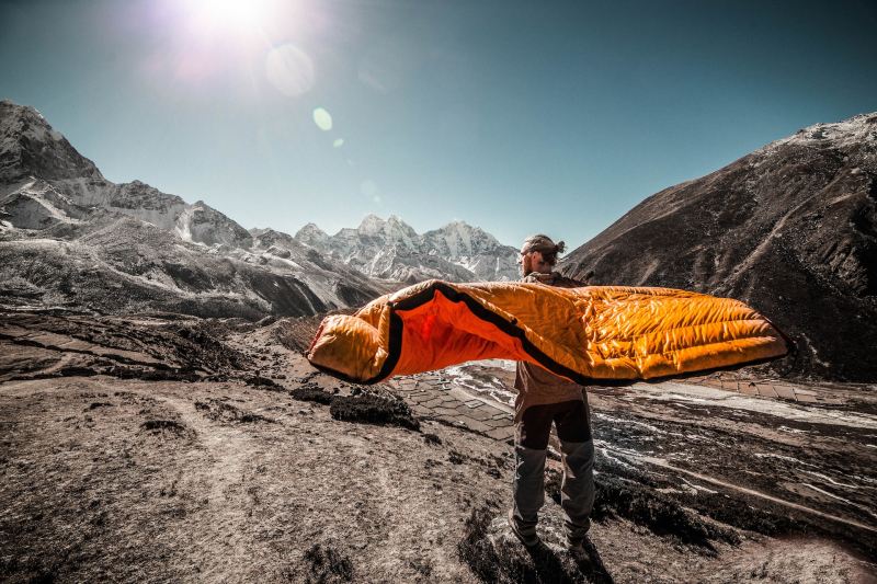 A man stands on the mountain with a sleeping bag around him.