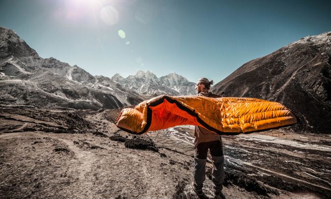 A man stands on the mountain with a sleeping bag around him.