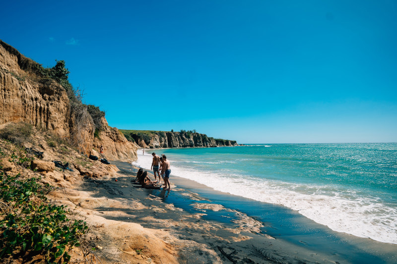 Group of people enjoying the sun and waves at Puerto Rico's Playa Negra black sand beach.