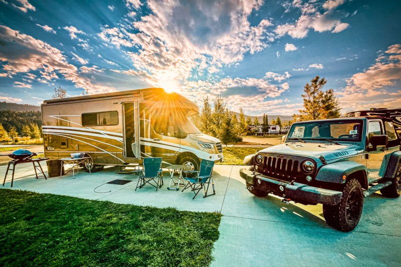 An RV and a Jeep at a campground with the setting sun in the background.