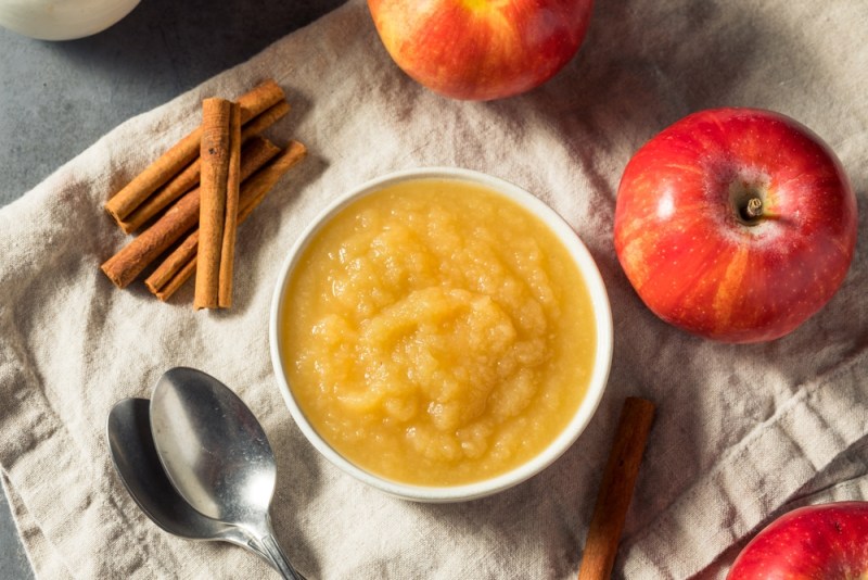 Applesauce in a bowl surrounded by cinnamon and apples.