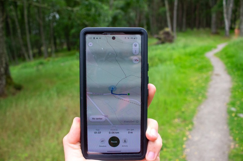 A person walks in the woods with their phone open and AllTrails running.