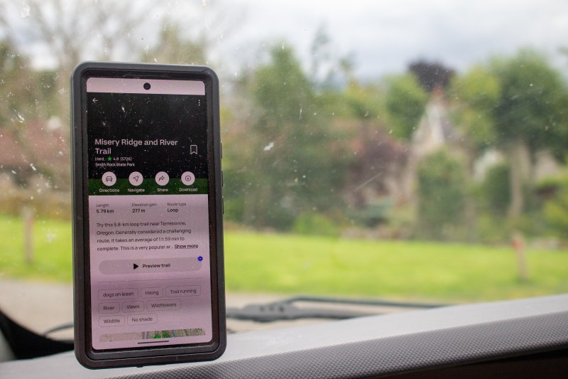 A phone with All Trails on the dashboard of a vehicle.