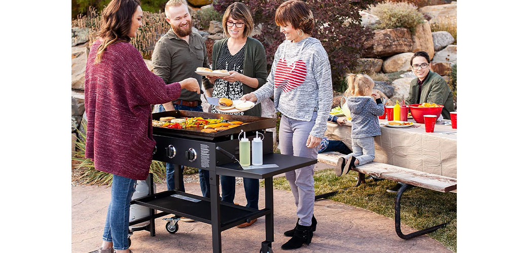 THe Blackstone 36-inch Gas Griddle Cooking Station in a yard with people around it cooking and enjoying themselves.