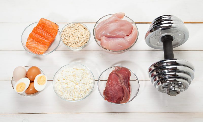 Protein food sources on a surface next to a bar bell