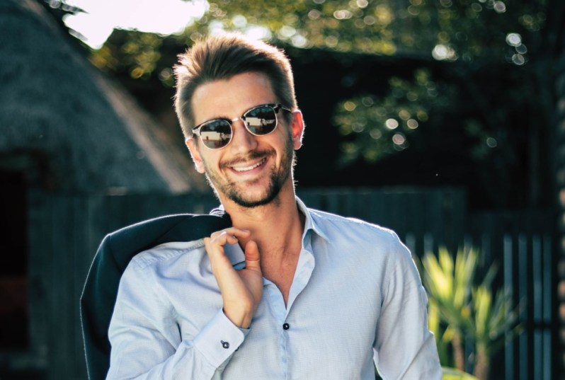 Man in round sunglasses with jacket on his shoulder