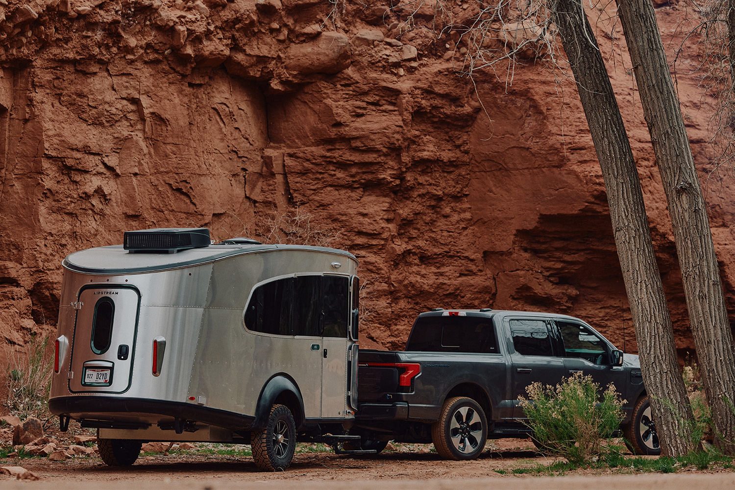 Black pickup truck towing an REI Co-op Special Edition Basecamp 20X travel trailer through a desert landscape.