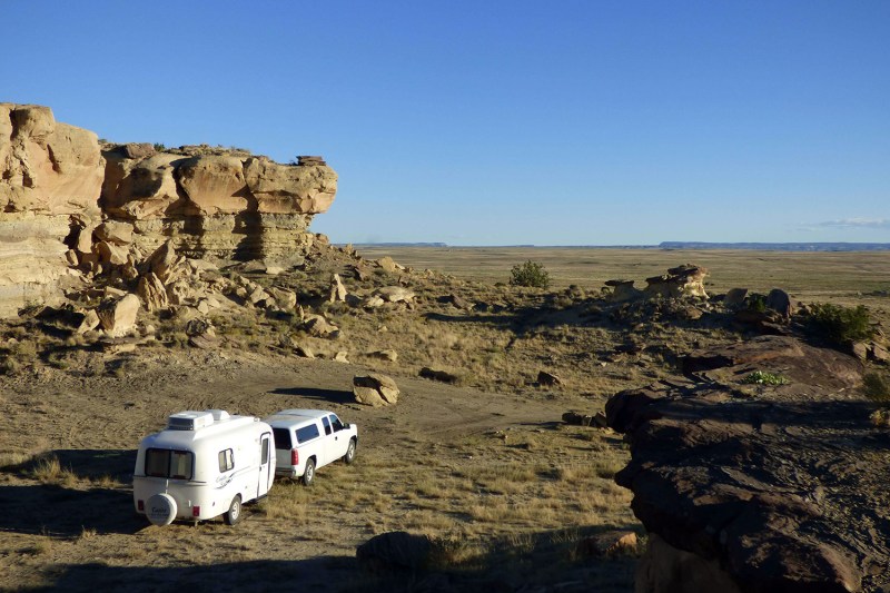 White pickup truck towing a Casita fiberglass travel trailer toward a desert cliff.