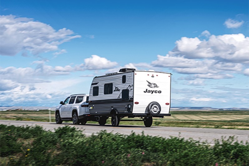 White SUV towing a Jayco travel trailer down a country road.