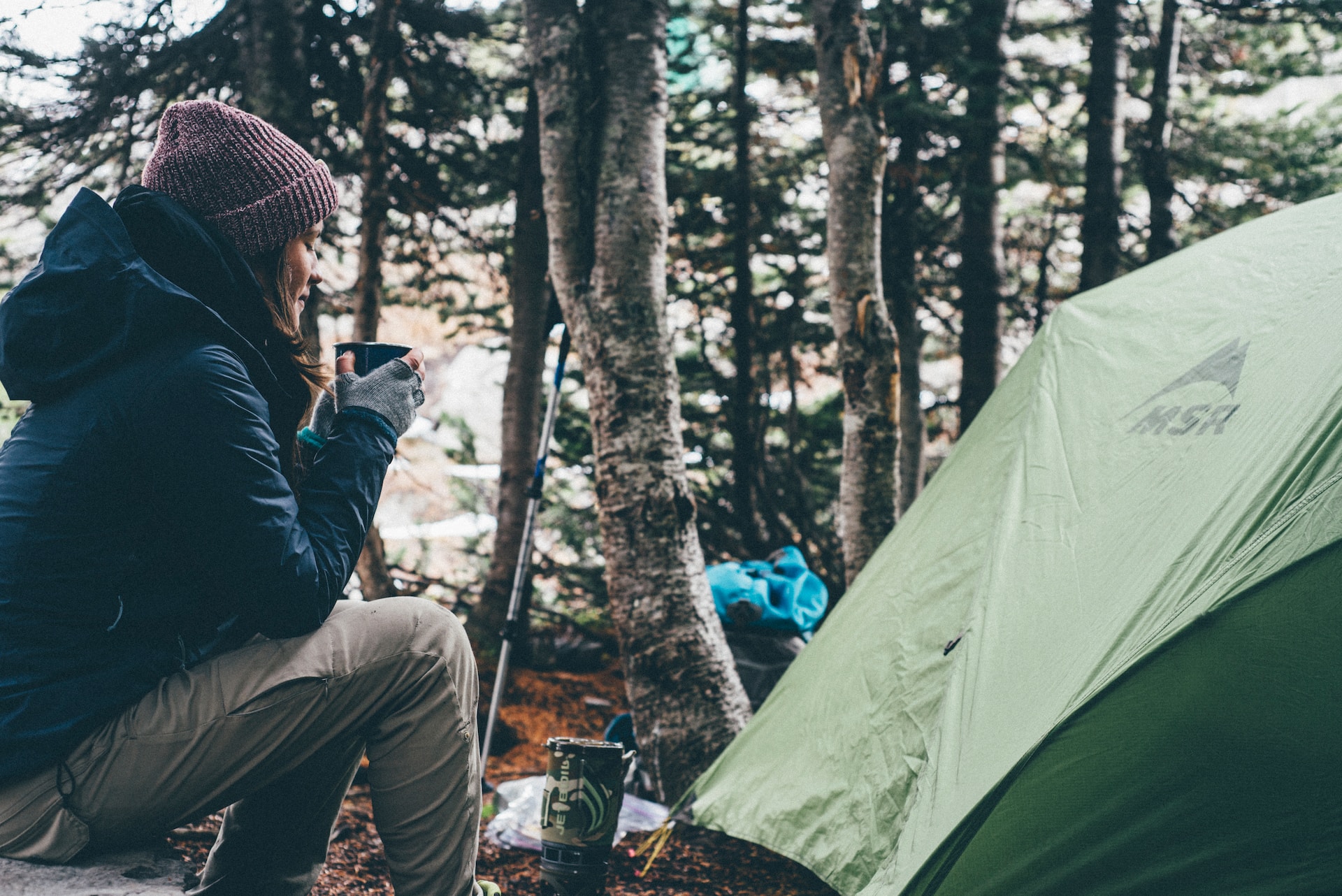 Young woman enjoying a cup of coffee, while sitting near a tent in the outdoors.