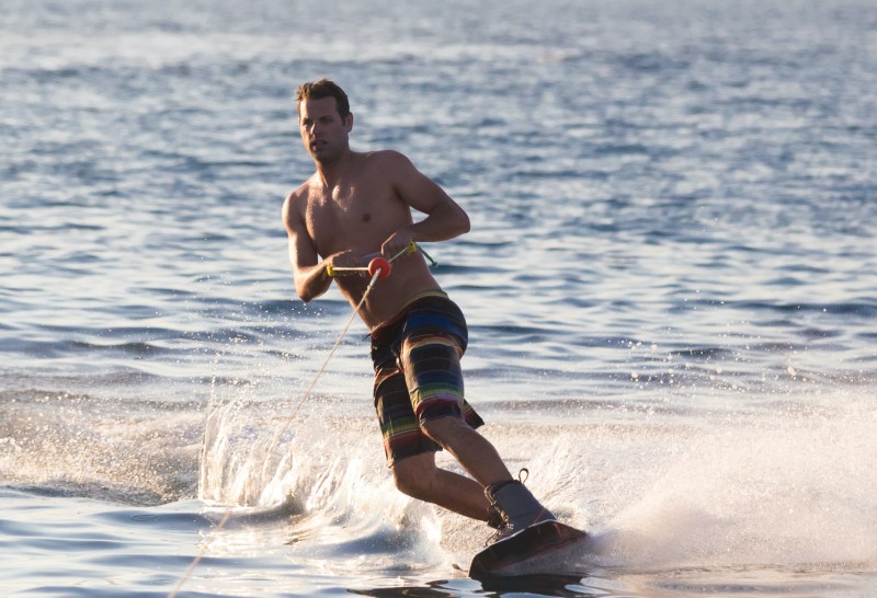 Wakeboarder in colorful shorts riding in sunset.