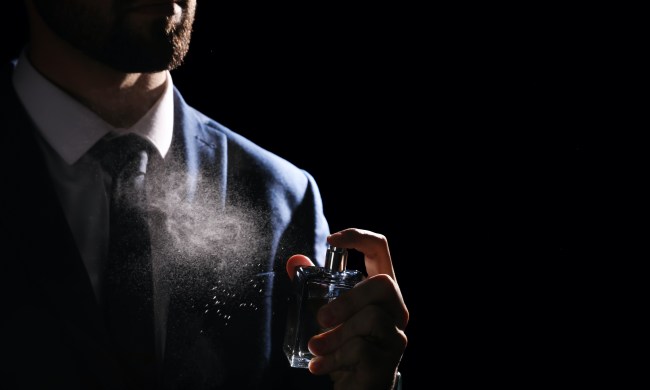 Man spraying luxury perfume on black background, closeup