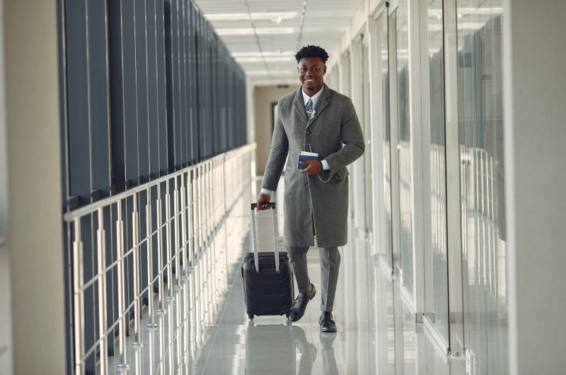 Well-dressed man rolling a luxury carry-on bag through a private plane terminal hallway