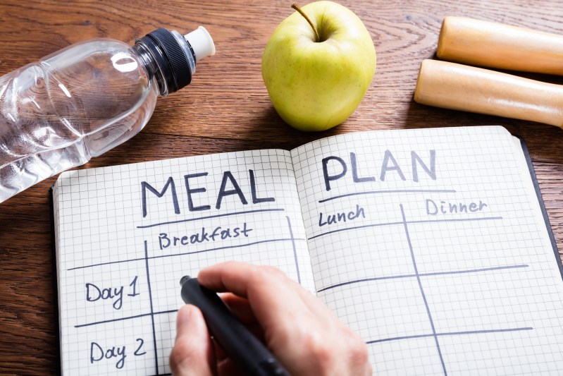 Person writing in notebook that has a meal plan template inside.