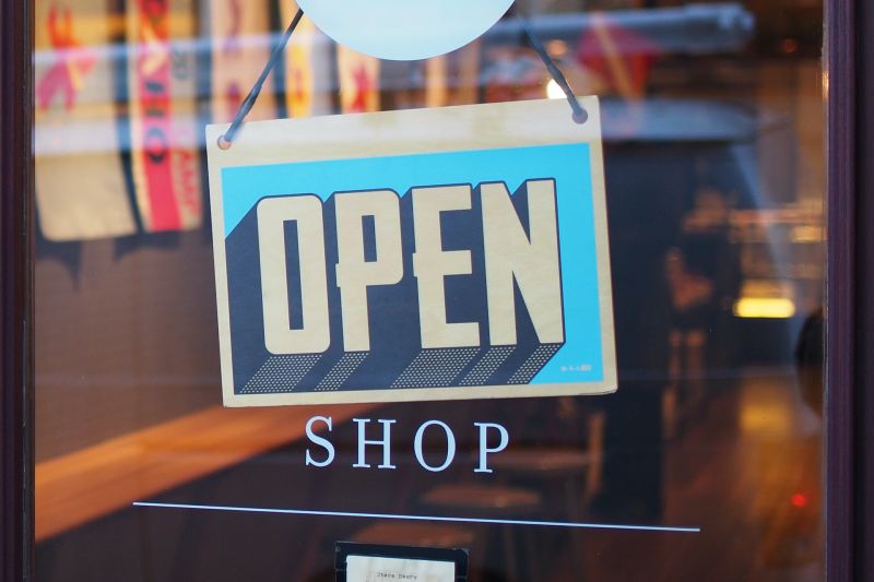 Gray and blue "OPEN" sign hanging on a the front door of a small shop.