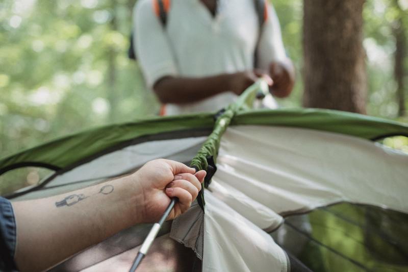 Closeup of two friends setting up a tent in the woods.