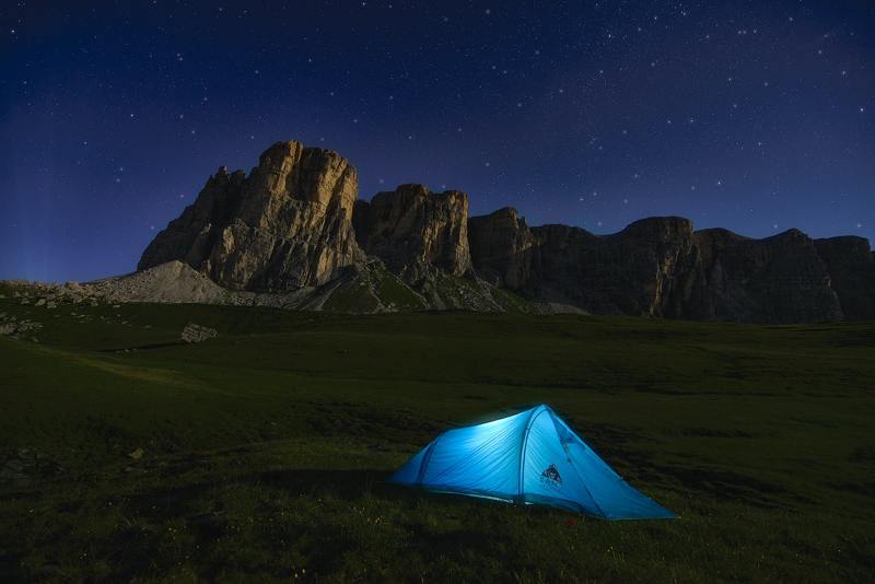 Lone blue tent lit from the inside in a desert landscape at night.