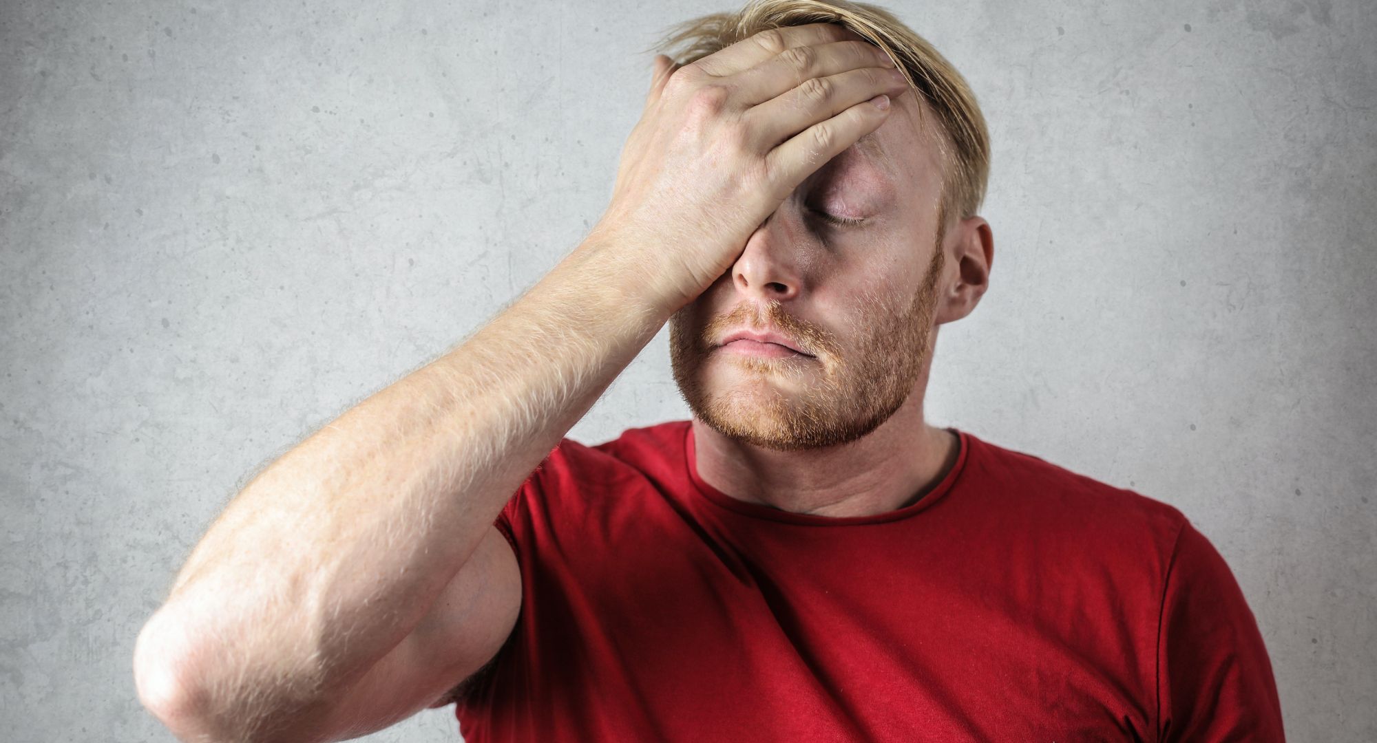 White man in a red shirt with his hand on his head