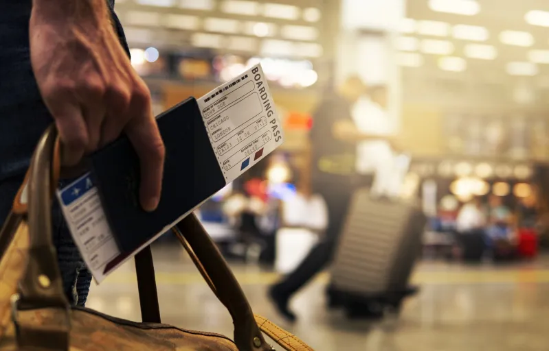 A closeup of a man's hand holding a boarding pass and carryon bag