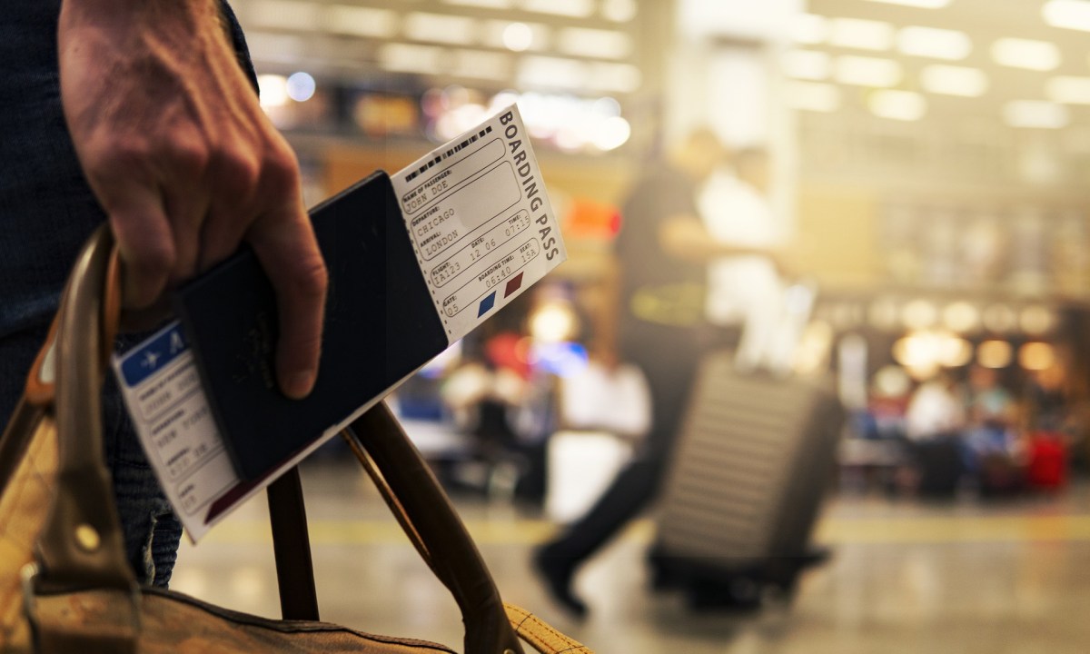 A close-up of a man's hand holding a boarding pass and a carry-on bag