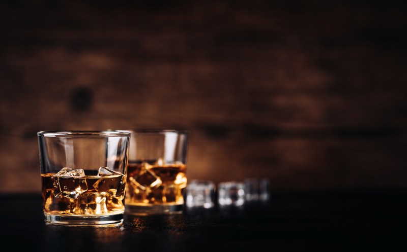 Whisky, whiskey, bourbon or cognac with ice cudes on black stone table and wood background