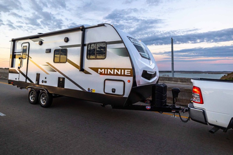 White pickup truck towing a Winnebago Minnie Winnie travel trailer over a bridge.
