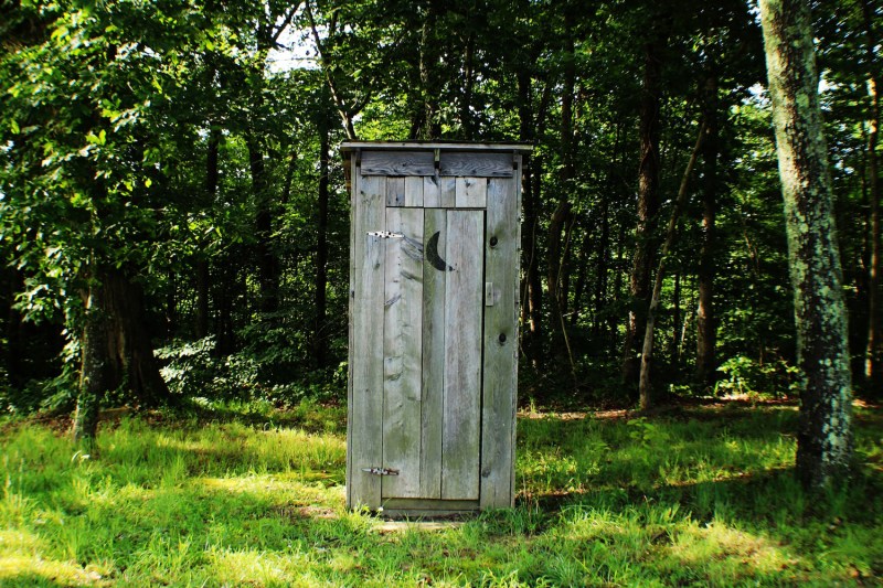 A wooden outhouse with a crescent moon cutout on the door.