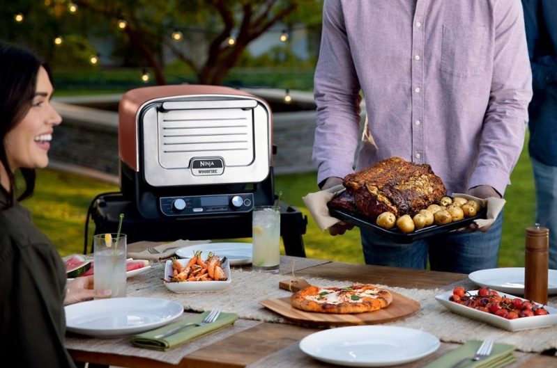 Ninja Woodfire 8-in-1 Outdoor Oven with Pizza in oven against a white background and accessories