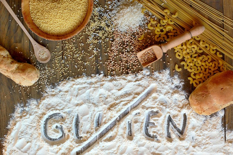 Gluten free cereals corn, rice, buckwheat, quinoa, millet, pasta and flour with scratched text gluten on brown wooden background,overhead horizontal view