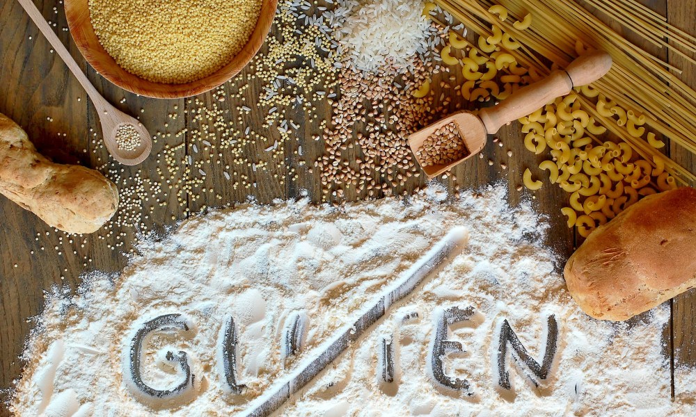 Gluten-free cereals corn, rice, buckwheat, quinoa, millet, pasta and flour with scratched text gluten on brown wooden background,,overhead view