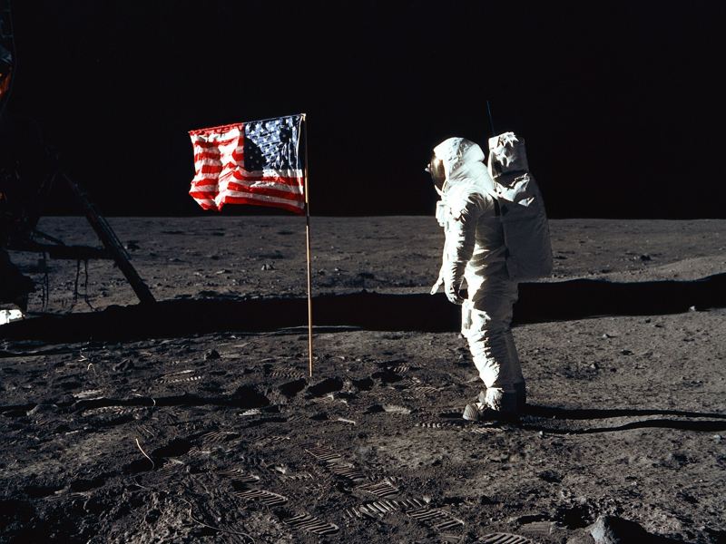 Buzz Aldrin en la luna de pie frente a la bandera estadounidense.
