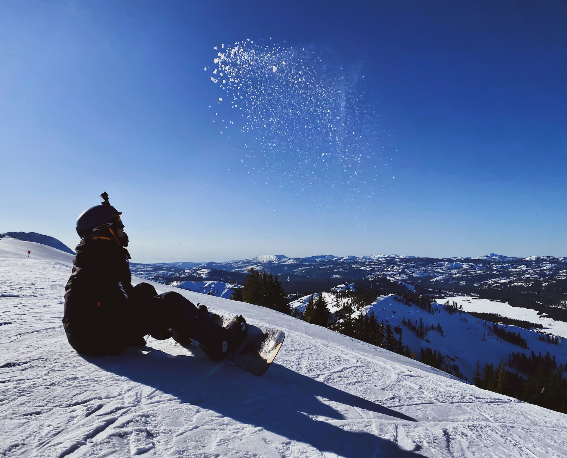 A snowboarder with an action camera on their head sits on the groomer.