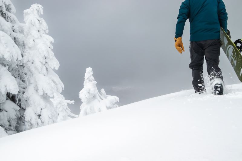 A man walks up a mountain in deep snow with a snowboard.