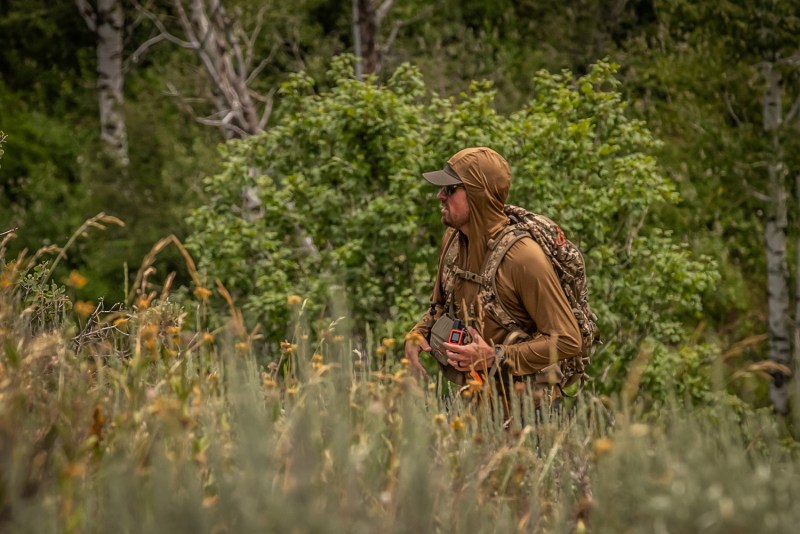 Man hiking through high grass in a Sitka Gear tan hoodie.