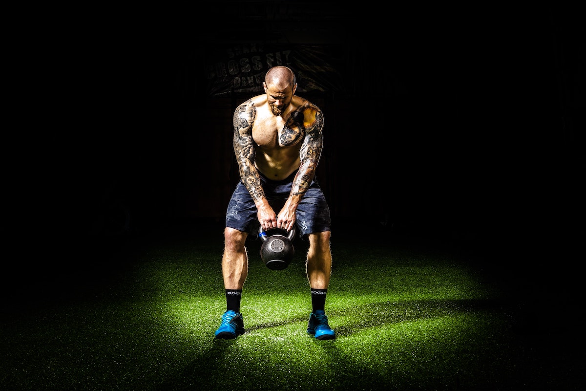 a man on a dark field with a spotlight on him lifting a kettlebell