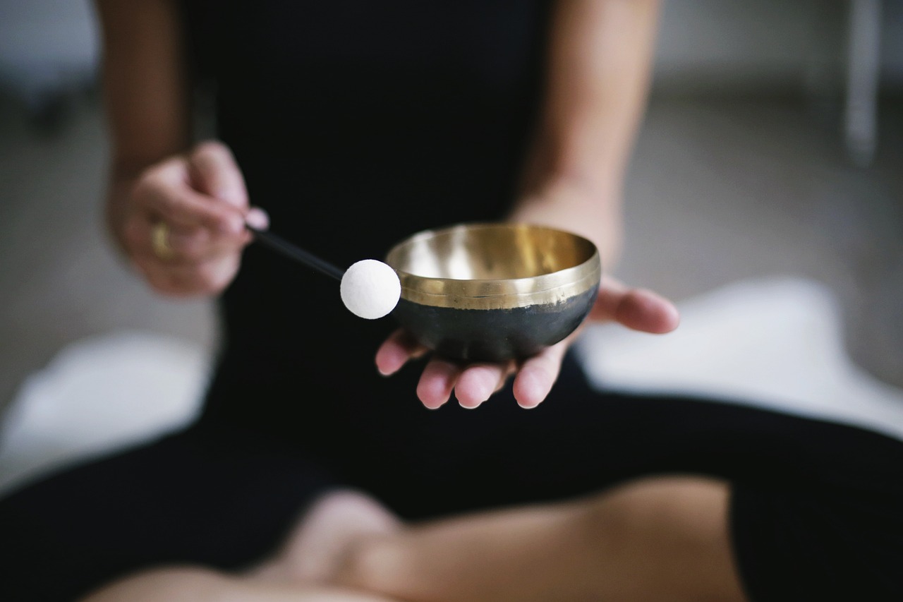 Person sitting cross legged on the ground holding a sound bowl.