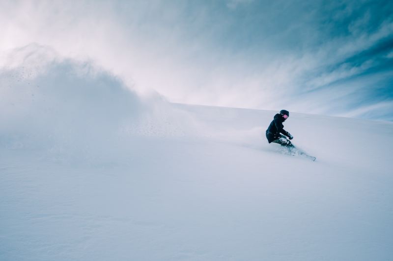 A person snowboarding in deep powder with clear skies behind them.
