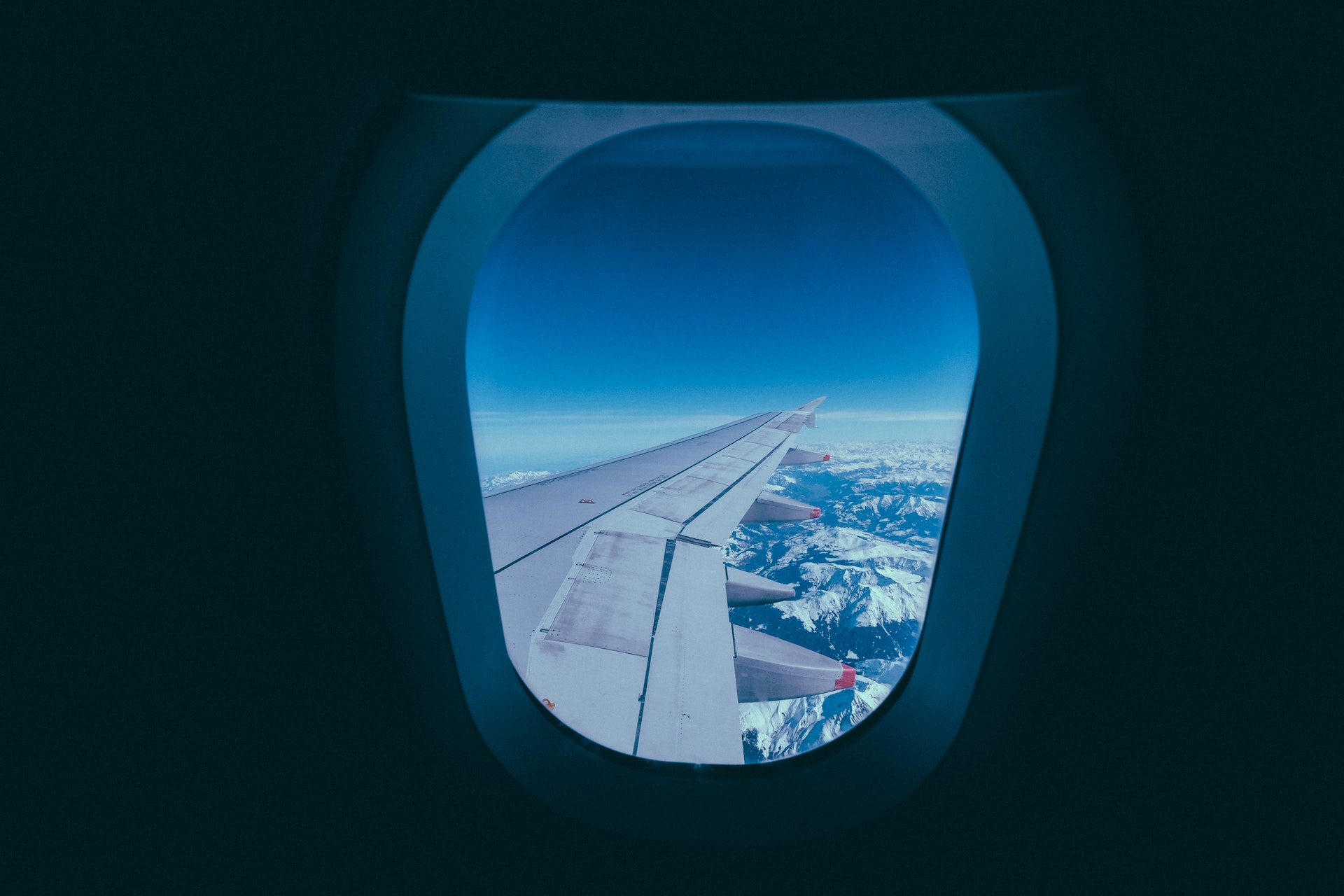 The view looking out of an airplane window into the clouds with mountains below