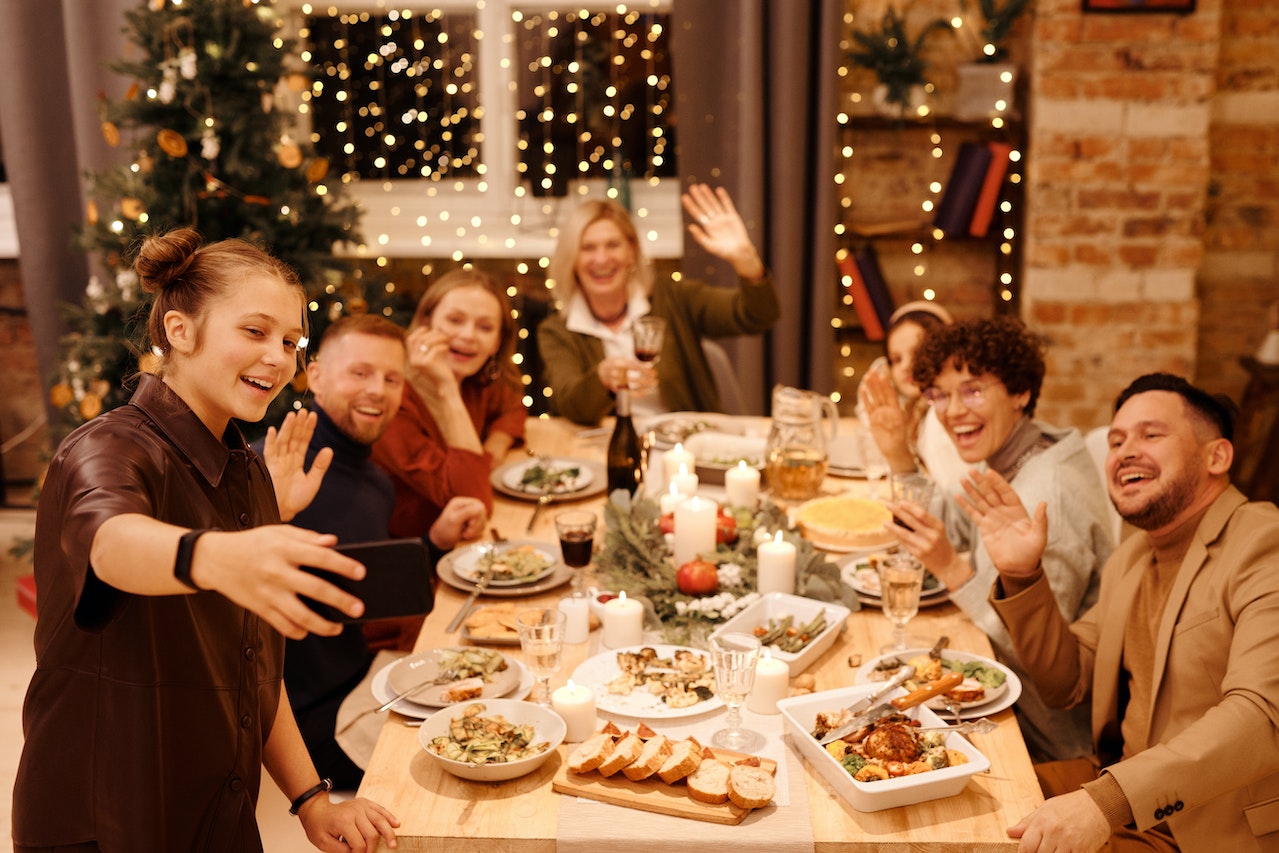 Family gathered around a holiday dinner table taking a group selfie and waving